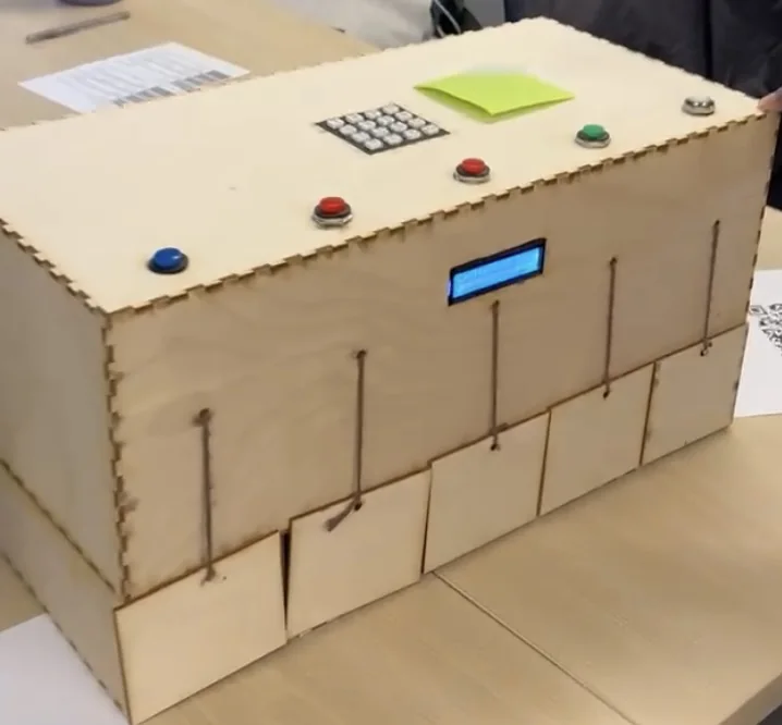 Prototype 2: the unpainted laser-cut plywood box with a keypad and buttons on top, an LCD, and five string-pulled doors